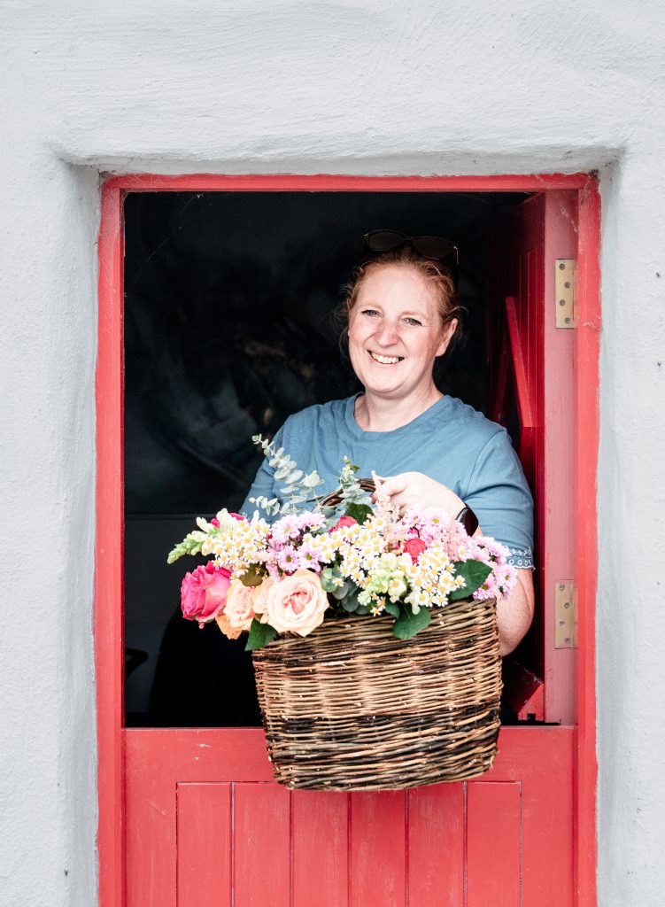 Lynda with a Basket of fresh cut flowers standing in a red half door